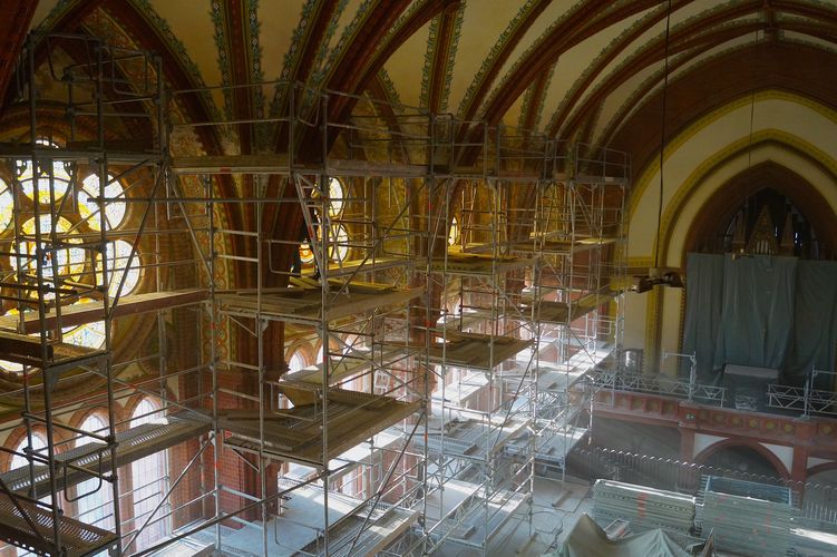 Kircheninnenraum mit leuchtenden Glasfenstern, davor Baugerüste