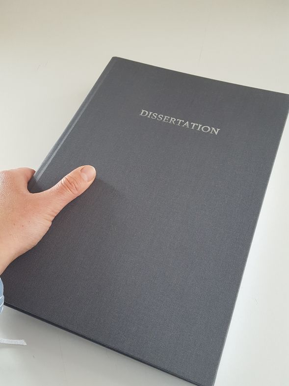 Eine Hand hält ein graues Buch mit der Aufschrift "Dissertation".