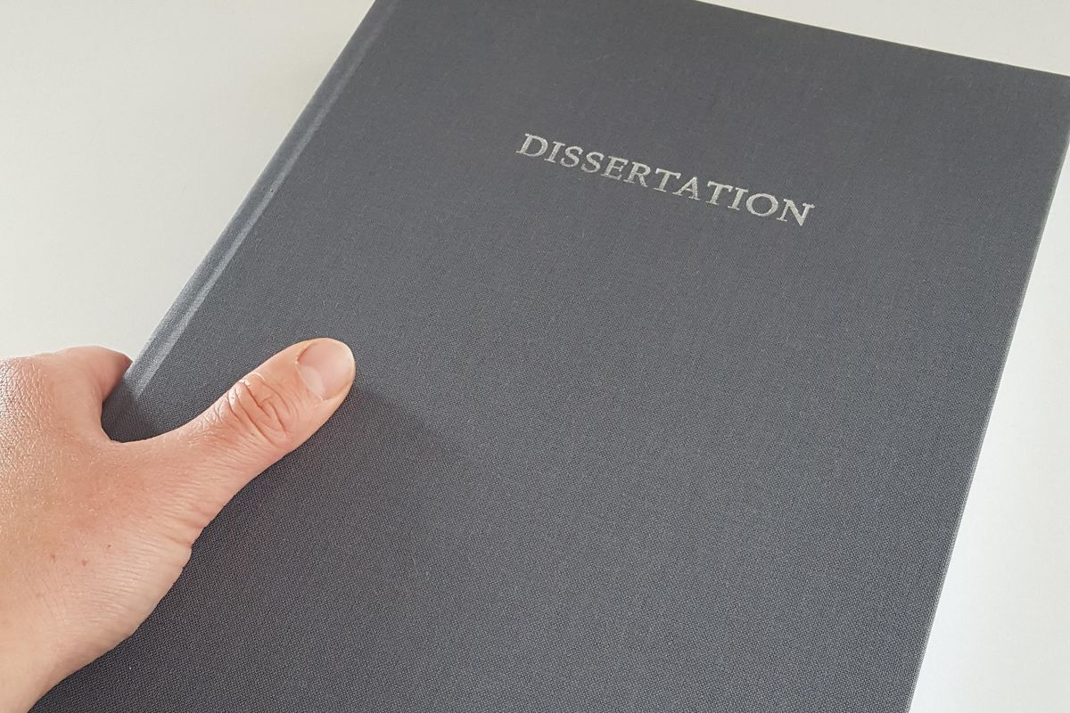 zur Vergrößerungsansicht des Bildes: Eine Hand hält ein graues Buch mit der Aufschrift "Dissertation".