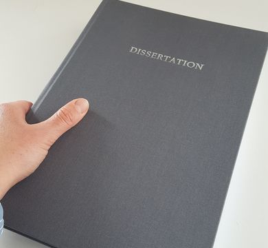 Eine Hand hält ein graues Buch mit der Aufschrift "Dissertation".