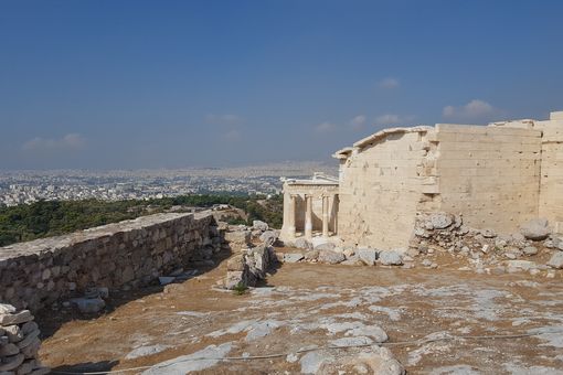 Blick von der Akropolis auf die Stadt Athen, Foto: Nicole Oesterreich. Auf der rechten Seite befinden sich griechische Tempelruinen, links eine Mauer. Im Hintergrund eine Stadt und blauer Himmel mit wenigen Wölkchen.