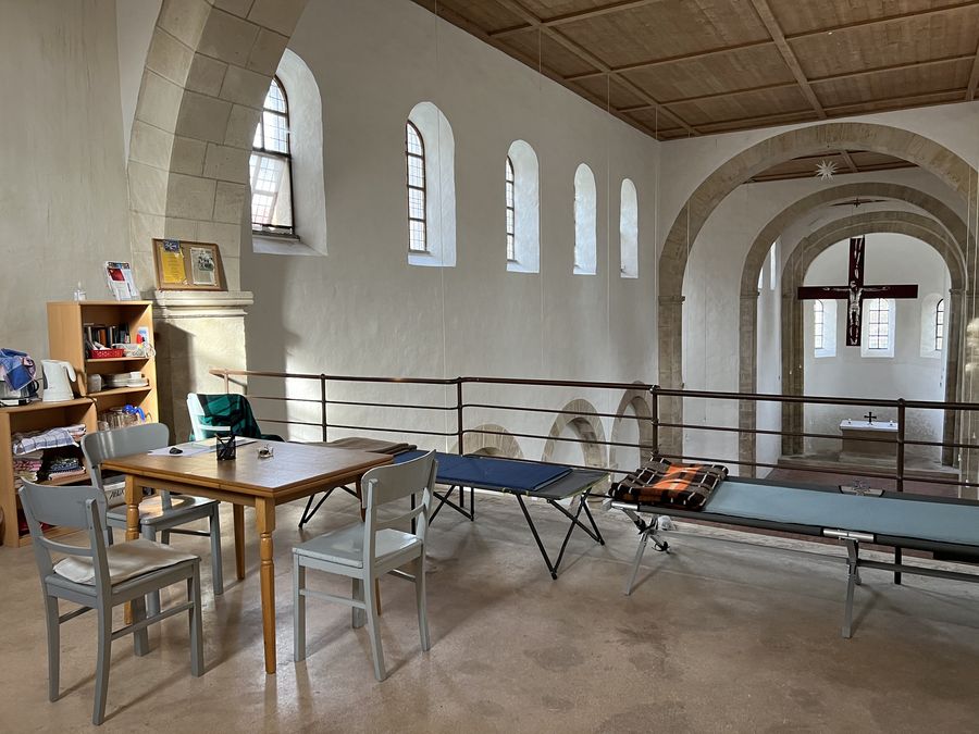 Tisch und Stühle, einfache Liegen mit Blick von der Empore in den romanischen Kirchenraum