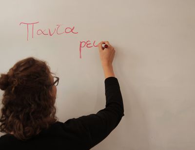 Eine Studentin schreibt an einem Whiteboard mit einem roten Stift. Dort stehen die Worte panta rei. Das ist Altgriechisch und heißt alles fließt.