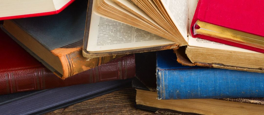 Bücher mit verschiedenfarbigen Einbänden liegen unsortiert und zum Teil aufgeschlagen übereinandner.