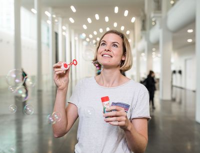 Eine Frau in einem großen Raum, die Seifenblasen pustet. Bildunterschrift: Studienstart, Foto: Christian Hüller.