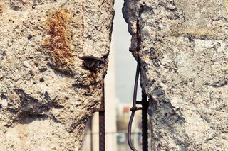 Das Foto zeigt ein Stück von der Berliner Mauer. In der Mauer ist ein Loch geschlagen. Auf der anderen Seite sieht man die Rückseite eines alten Autos.