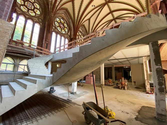 Baustelle mit Rohbau einer geschwungenen Treppe im Kirchenraum