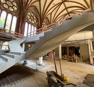 Baustelle mit Rohbau einer geschwungenen Treppe im Kirchenraum