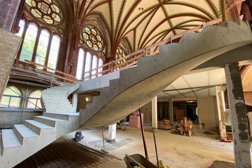 Baustelle mit Rohbau einer geschwungenen Treppe im Kirchenraum