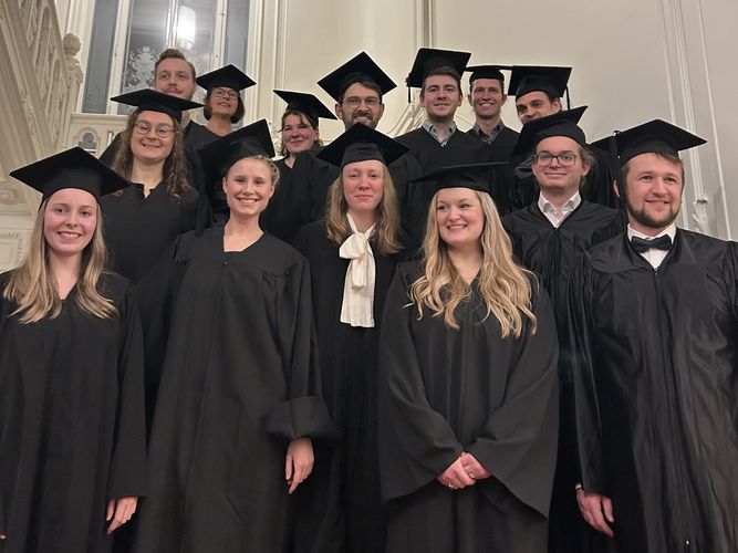 Foto: Gruppenbild im Treppenhaus des Rektorats in Studententalaren und mit Doktorhüten