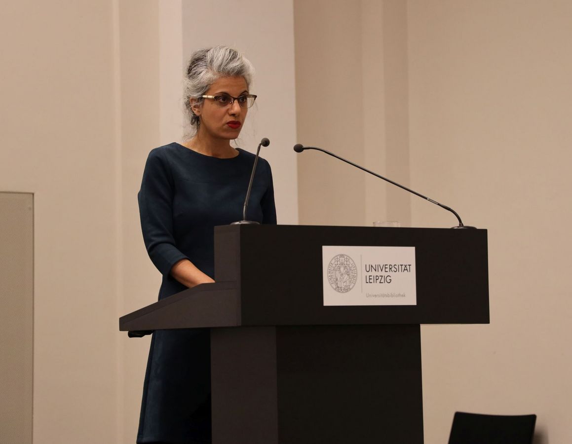 zur Vergrößerungsansicht des Bildes: Yemima Hadad bei der Antrittsvorlesung, Foto: Frank Lütze. Eine Frau mit Brille im blauen Kleid an einem Pult beim Vortrag.