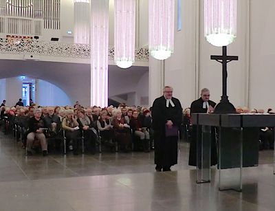 Zwei Männer im Talar vor dem Altar in einer gut gefüllten Kirche.