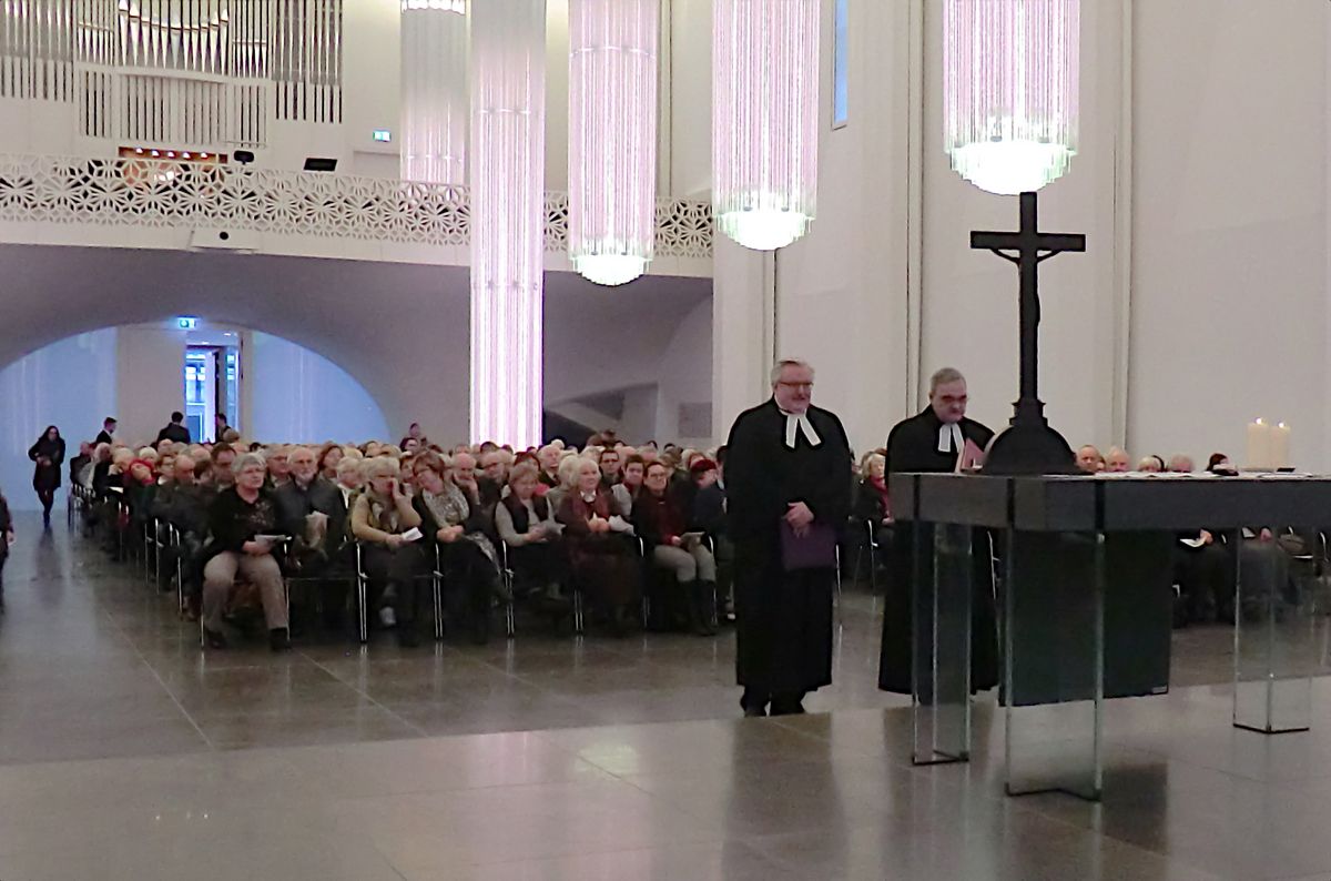 zur Vergrößerungsansicht des Bildes: Zwei Männer im Talar vor dem Altar in einer gut gefüllten Kirche.