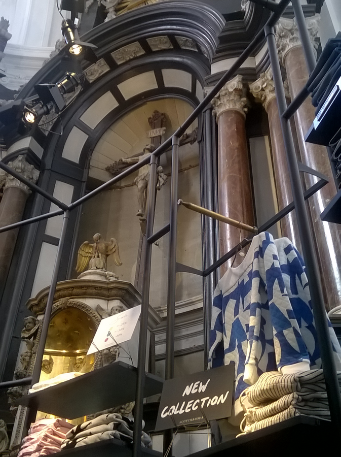 Regal mit Bekleidung vor einem Hochaltar, Bekleidungsgeschäft in einer ehemaligen Kirche in Belgien